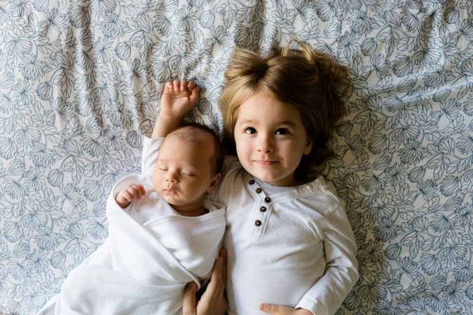 A newborn baby and toddler laying on the bed, looking up.