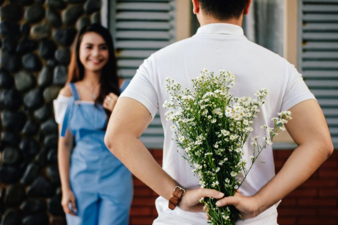 A man holding flowers behind his back while a lady greets him.