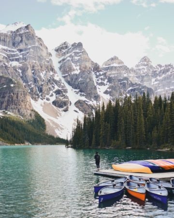 A man standing on a dock in a lake looking at the mountains in the distance.