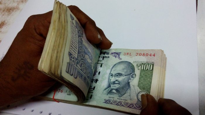 A person counting Indian Rupees wrapped in a rubber band.