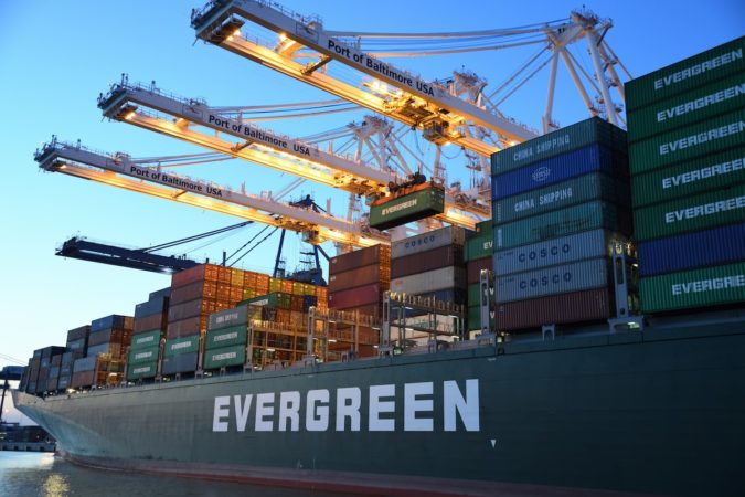 A shipping vessel docked at a shipping port being loaded with containers.