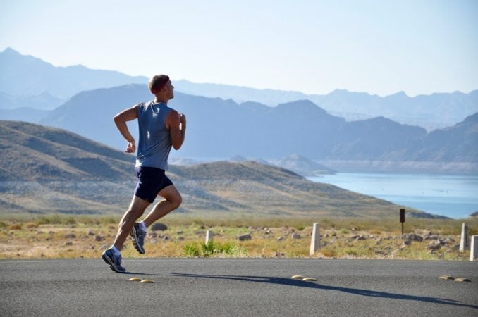 A man running down the road with a lake and some mountains behind him.