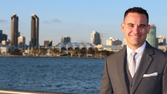 An insurance broker smiling in the foreground of a city.