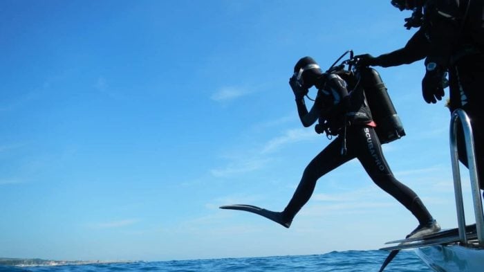 A person wearing scuba diving equipment stepping off a boat and into the water.