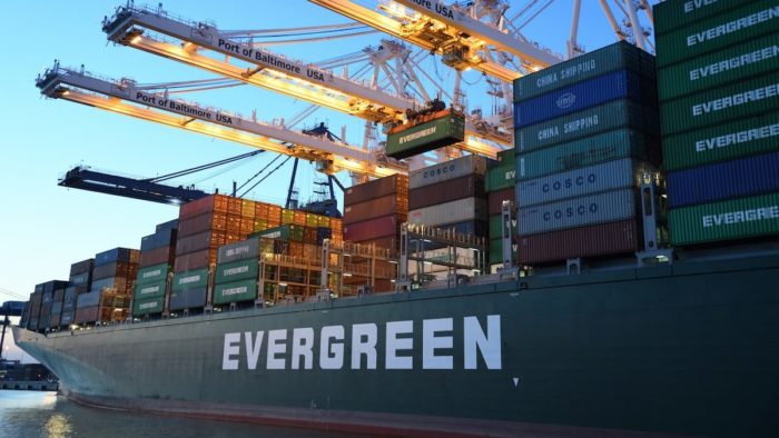 A shipping vessel docked at a shipping port being loaded with containers.