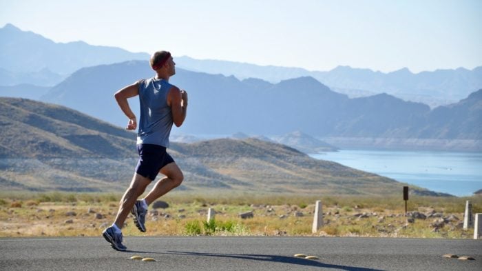 A man running down the road with a lake and some mountains behind him.