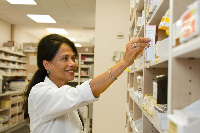 A pharmacist reaching for medicine on a shelf.