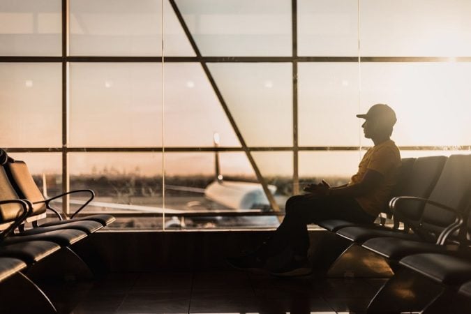 A man waiting in an airport with a plane outside the window. 