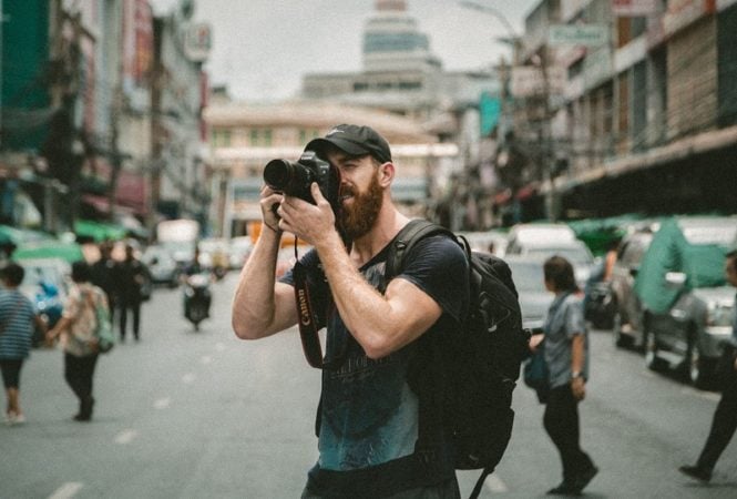 A male tourist in Asia with a DSLR camera setting up a shot.