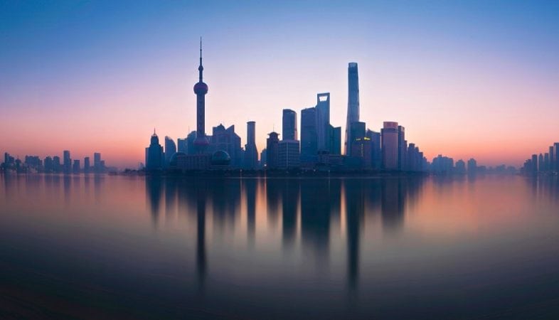 The Shanghai skyline at sunset in pink and blue with a reflection ont he river.