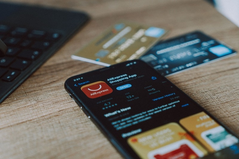 A phone on a desk with the AliExpress app download screen visible. 