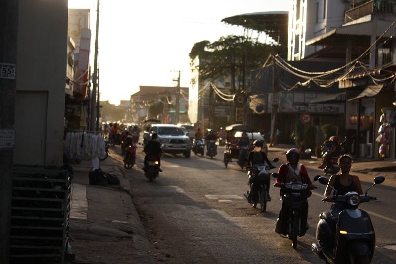 A photo of a small street in Cambodia with scooters and cars. 