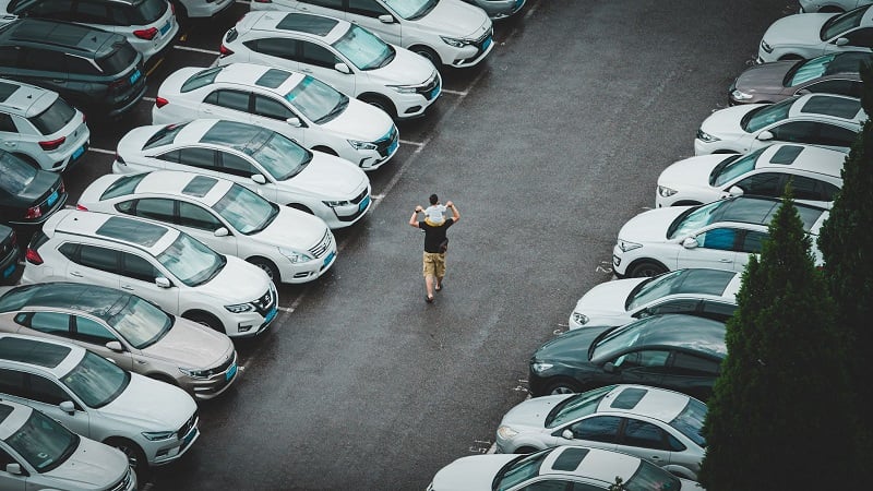 A photo of a man with a child on his shoulders taken from above as they walk through a used car lot in China. 