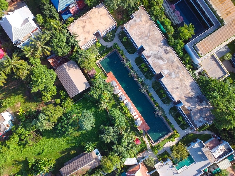 An overhead photos looking down on a pool and greenery surrounded villas in Cambodia.