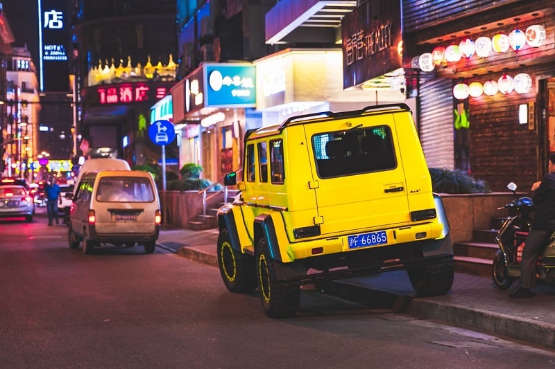 A photo of a bright yellow jeep parked half on the sidewalk in China. 