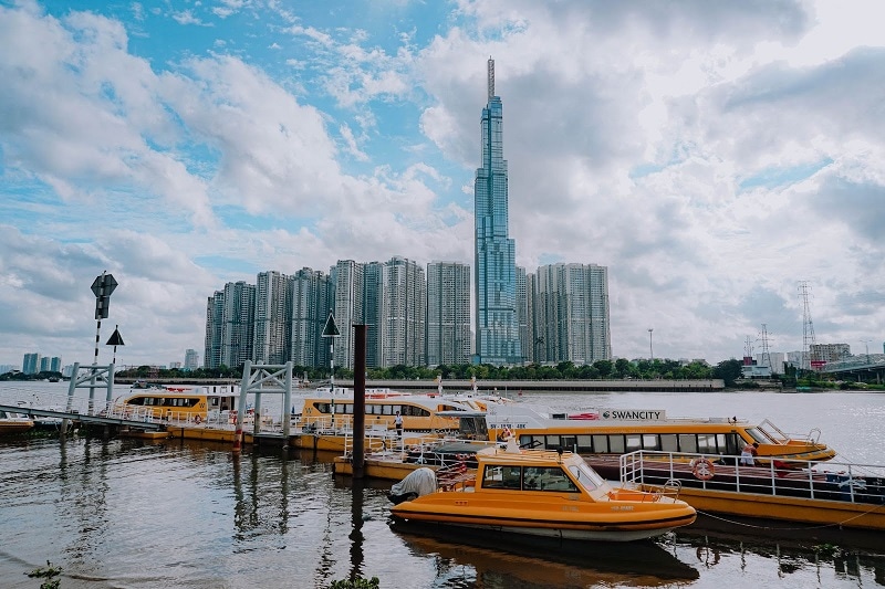 Ho Chi Minh City, Vietnam. View of the water with skyscrapers in the background and yellow small ferries in front.