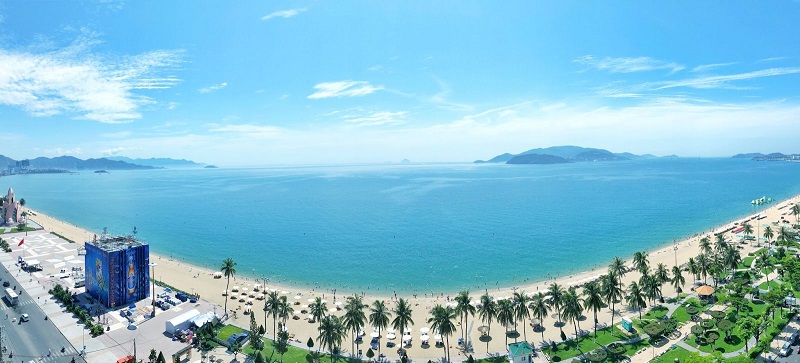 A fish-eye photo view of the beach and ocean of Nha Trang. Palm trees line the white sand. 