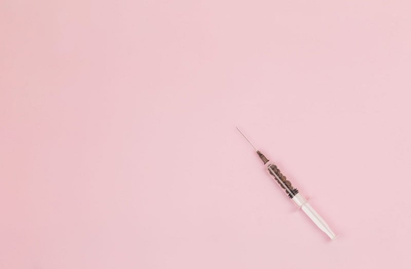 A medical syringe on a pink background. 