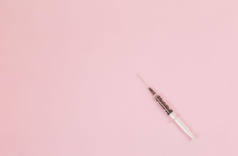 A medical syringe on a pink background.