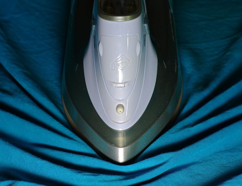 Close-up photo of an iron moving across blue fabric.
