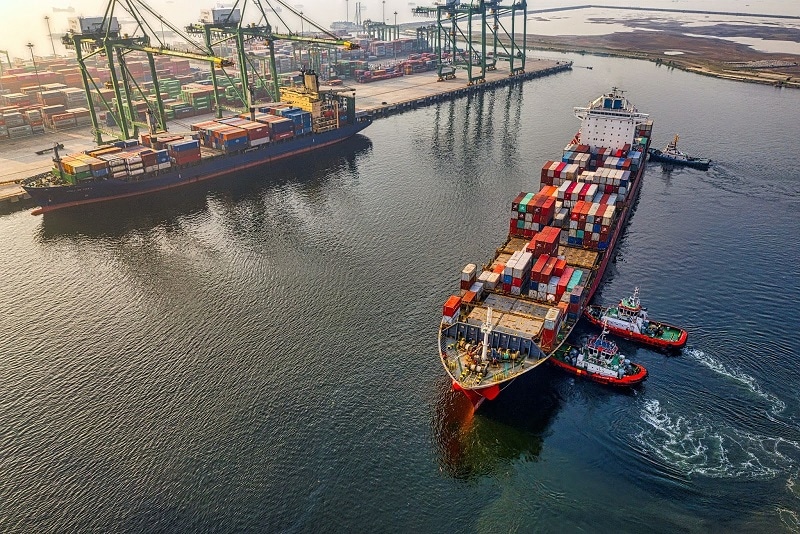 A large cargo ship full of containers near a post.