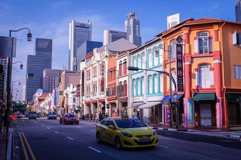 Singapore's old and new parts of town visible in one street photo with cars and colouful shops. 
