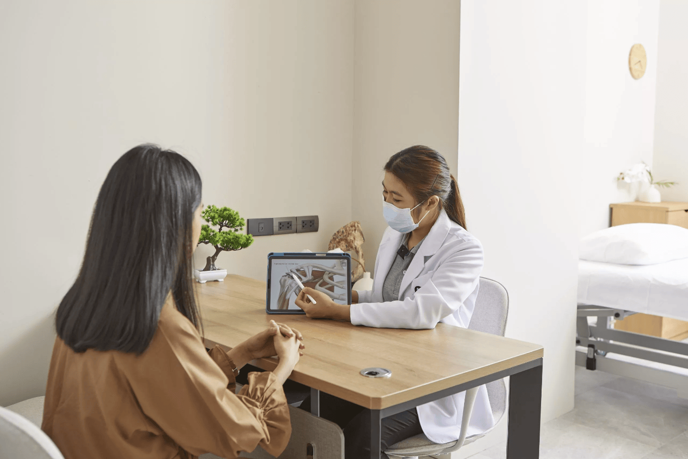 A physiotherapist is showing a patient her shoulder injury on a tablet computer.