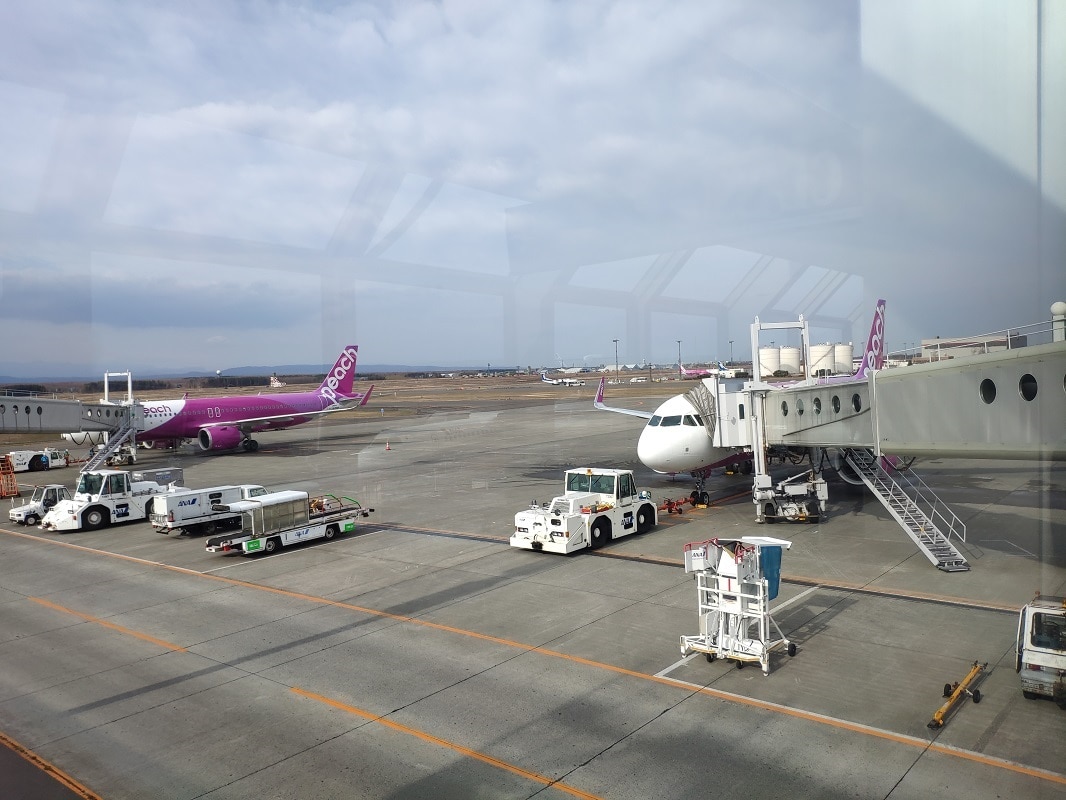 A photo out an airport window with planes and airport vehicles.