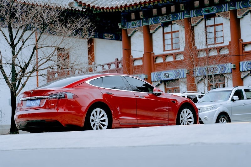 A photo of a brand new red Tesla in front of a traditional Chinese building. 