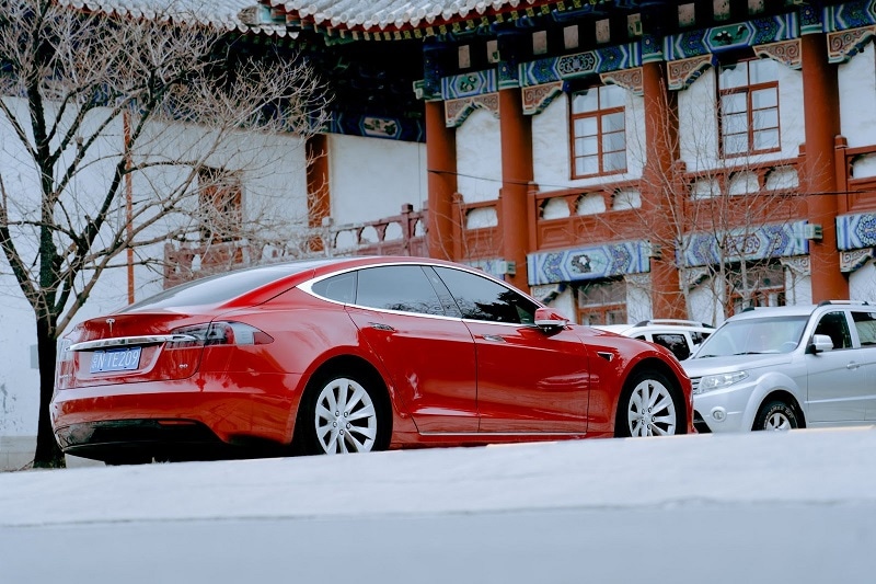 A photo of a brand new red Tesla in front of a traditional Chinese building. 