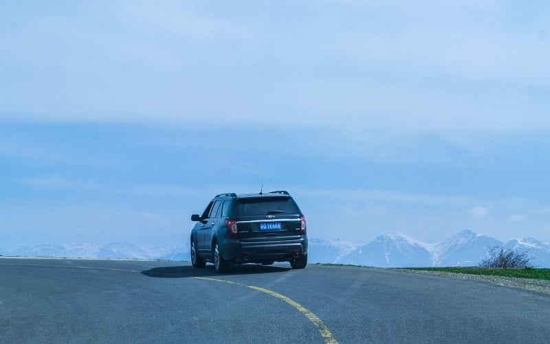 A photo of a black SUV with a Chinese license plate driving in the mountains. 