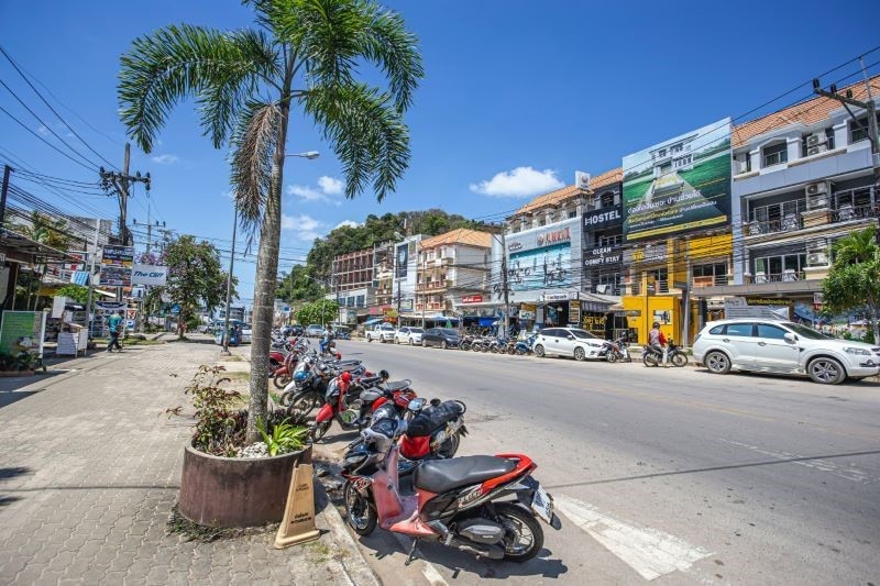 A Thai street with a line of motorcycles parked by the sidewalk. 