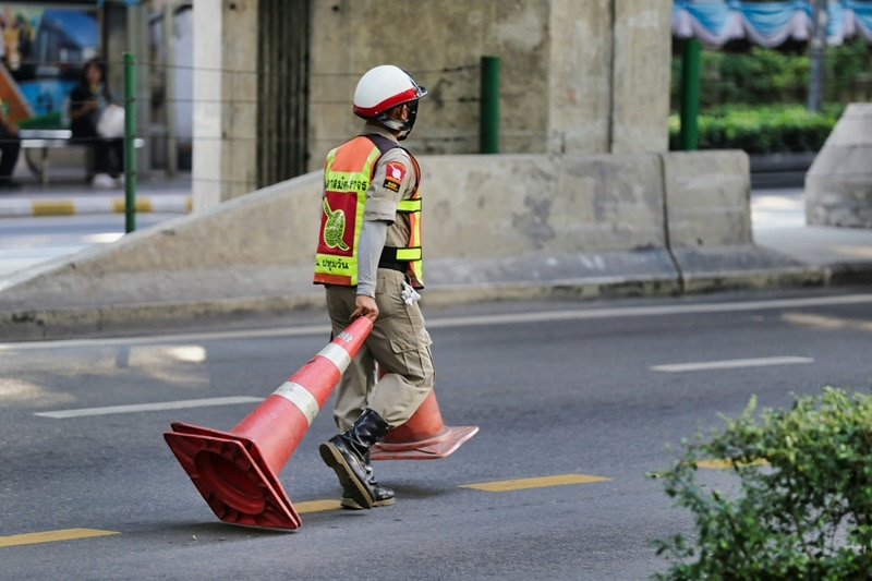 A Bangkok traffic police officer in uniform, dragging cones. 