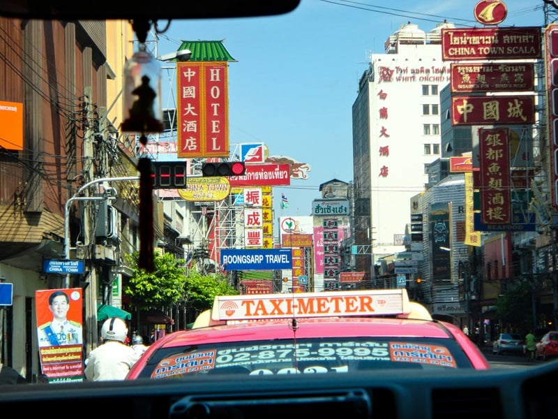 A pink Bangkok taxi driving down a busy street. 
